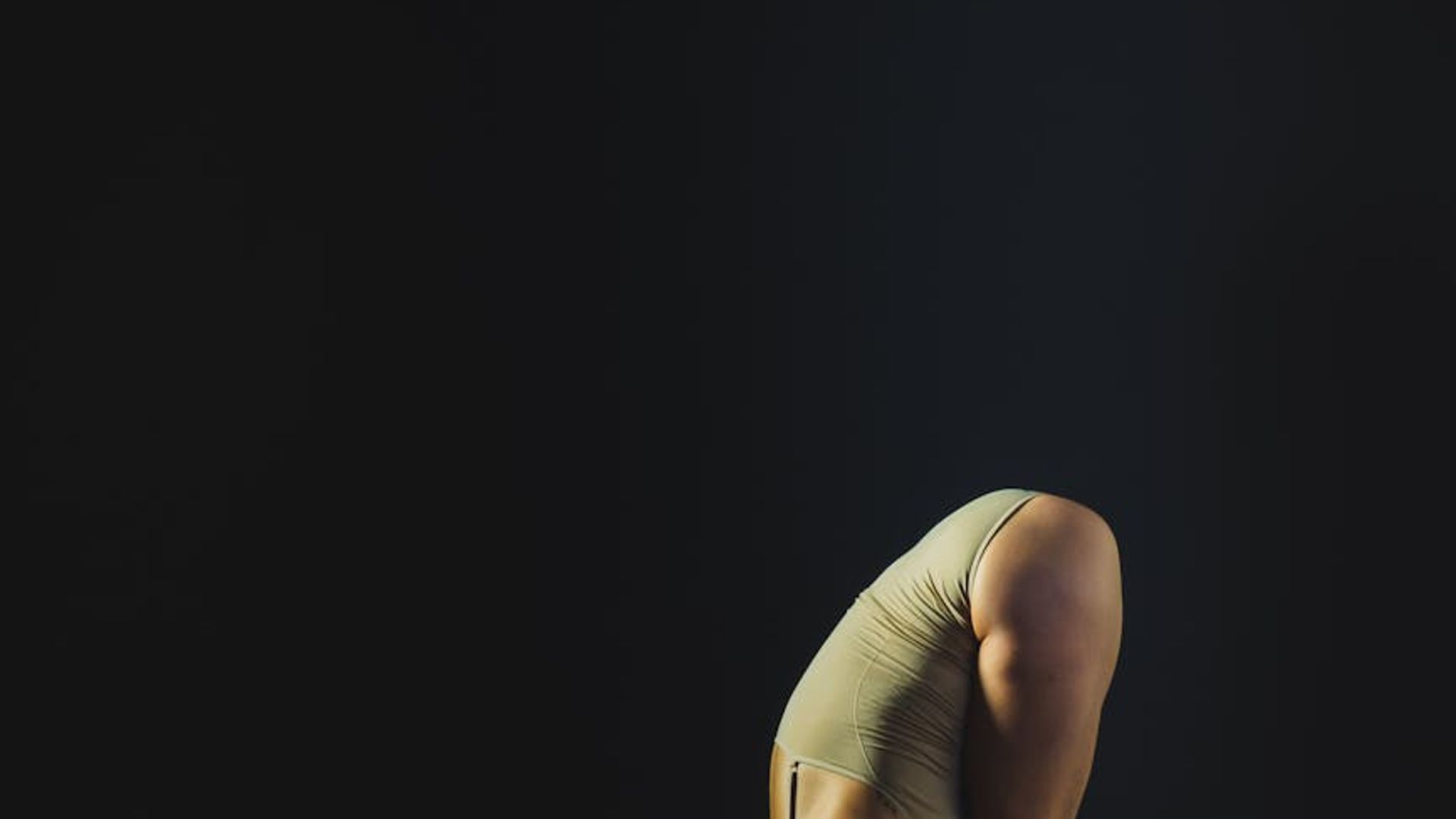 Person performing elegant yoga movements in a dark studio.